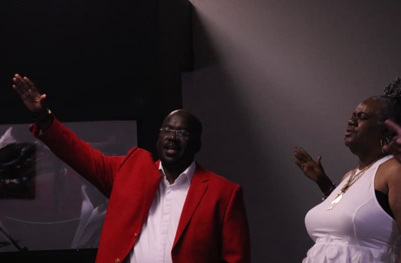 Two members praising with arms lifted during a service at Advance Church